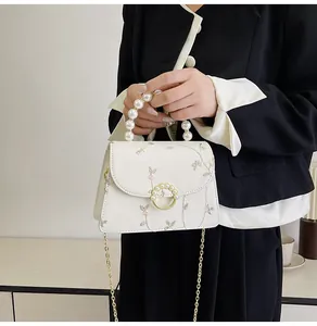 Detail of cream crossbody bag with floral pattern, pearl handle, and gold chain strap