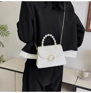 Close-up of a white crossbody bag featuring a pearl handle and gold chain strap
