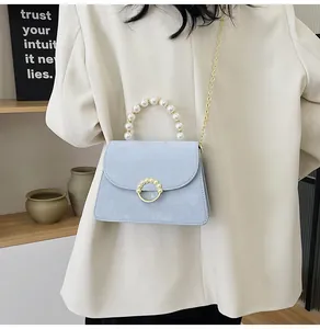 Detail of light blue crossbody bag with pearl handle and golden chain on beige blazer