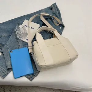 Flat lay of off-white canvas crossbody bag with adjustable strap and front pocket detail