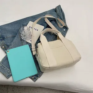 Detail of off-white canvas tote showing front pocket and detachable shoulder strap texture