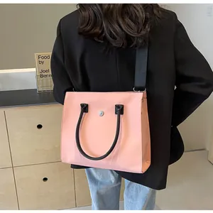 Detail view of pink tote bag with black handles and shoulder strap worn by a model