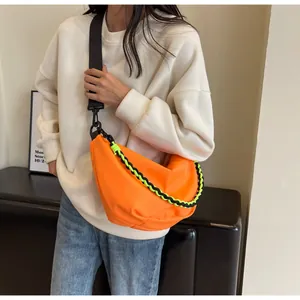 Detailed view of an orange crescent nylon bag with two-tone woven chain on a model