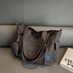 Detail of black canvas tote bag showing front zipper pocket and mini round hanging pouch