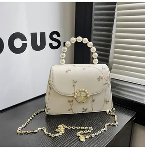 Detailed close-up of floral embroidery and pearl handle on the cream crossbody bag