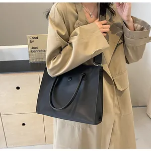 Detail of black leather tote bag with round metal buckle and wide adjustable shoulder strap
