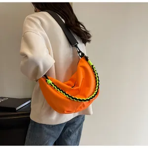 Street style shot of a bright orange nylon crescent bag with neon green rope detail