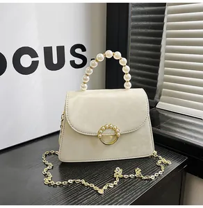 Detail of off-white leather crossbody bag with pearl handle and golden chain strap