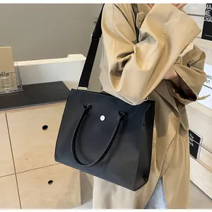Detail of minimalist black tote bag with wide strap worn with a khaki trench coat