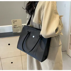 Close-up of black nylon tote bag with dual handles and adjustable shoulder strap shown in lifestyle setting