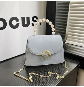 Detail of light blue crossbody bag with elegant pearl handle and gold chain strap