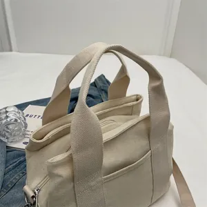 Detail of off-white canvas tote bag with adjustable shoulder strap and metal zipper closure