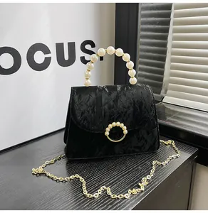 Detailed close-up of black pleated handbag featuring pearl handle and gold ring buckle