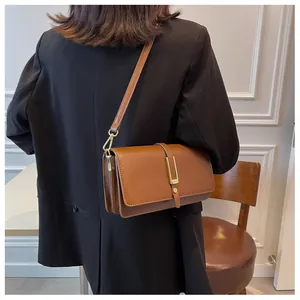 Detail of a brown leather crossbody bag with a gold buckle on a model in a modern room