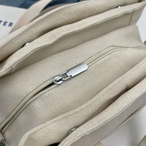 Detailed macro view of the silver zipper and beige canvas texture on the crossbody bag