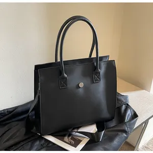 Detail of black PU leather tote bag featuring a silver round magnetic clasp and dual handles