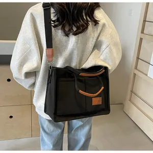 Vista laterale di una borsa tote in tela nera con manici in pelle marrone e tracolla