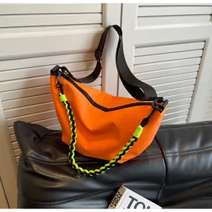 Detailed shot of the bright orange nylon moon bag with black wide strap and green tassel