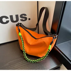 Detail of orange nylon dumpling bag with adjustable strap and green woven chain