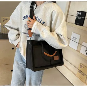 Dettaglio della borsa tote in tela nera con tasche anteriori e tracolla in nylon regolabile