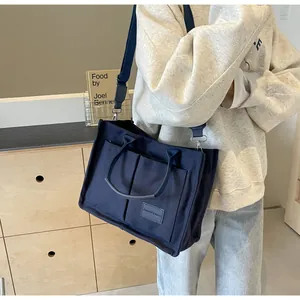 Dettaglio della borsa tote in tela blu scuro con tasche frontali ed etichetta in pelle