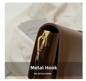 Detail shot of sturdy gold metal hook and fine stitching on a brown leather shoulder bag