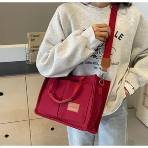 Dettaglio della borsa tote in tela rossa con etichetta in pelle e tracolla su una modella