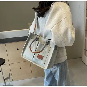 Dettaglio della borsa tote in tela grigio chiaro con manici in pelle marrone e logo