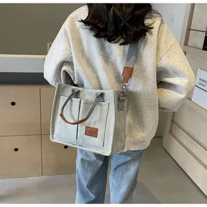 Dettaglio della borsa tote in tela grigio chiaro con finiture in pelle marrone e tasche