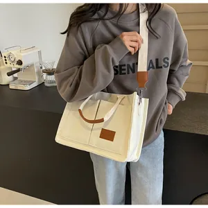 Borsa tote in tela bianca con manici in pelle marrone e tracolla regolabile in un caffè