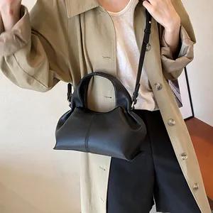 Detail of a black lychee texture crossbody bag styled with a khaki trench coat for a chic look