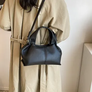 Detail of black PU leather handbag with matte lychee texture and pleated design on a trench coat