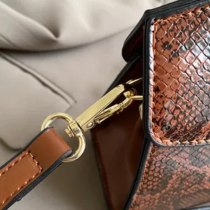 Makro-Detail einer braunen Handtasche in Schlangenleder-Optik mit goldenen Metallschnallen