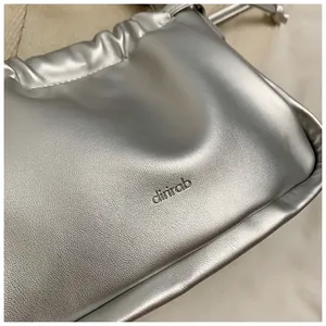Close-up of shiny silver pleated cloud bag with drawstring detail and branded logo