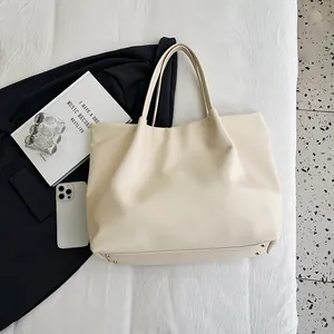 Flat lay of cream oversized tote bag showing metal feet and minimalist faux leather texture