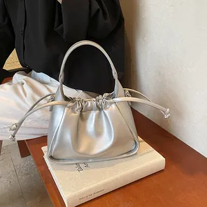 Silver metallic cloud handbag with drawstring ruched detail resting on a book