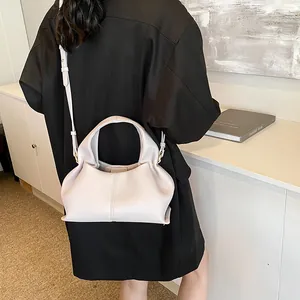 Minimalist beige leather shoulder bag shown on model with adjustable strap and soft folds