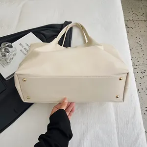 Detail shot of beige tote bag bottom featuring four protective golden metal studs