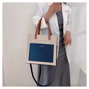Canvas tote bag with blue pocket and brown leather handles shown on shoulder by model