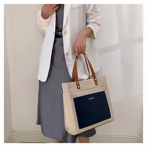 Detail view of canvas tote bag with contrast blue leather pocket and brown handles