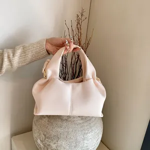 Detail of elegant pleated cream handbag with lychee texture and soft golden hardware
