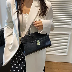 Detail einer eleganten schwarzen Handtasche mit Eidechsenprägung und Goldverschluss