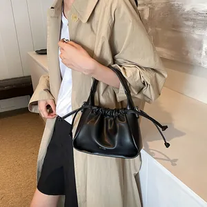 Detail shot of black pleated bucket bag with drawstrings on a beige trench coat