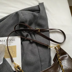 Detail of dark brown glossy leather bag with gold chain strap on grey blazer