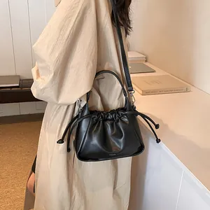 Detail view of black pleated drawstring bucket bag with handle and slim shoulder strap