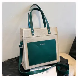 Detail of canvas tote bag showing contrast stitching, green pocket, and logo