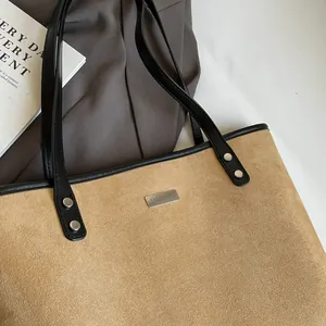 Detail of camel suede tote bag with black leather straps and silver metal logo plate