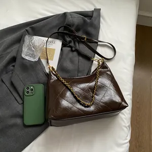 Detail view of quilted brown leather underarm bag with gold chain strap on fabric background