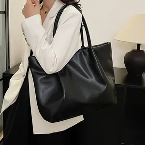 Detail of a large black faux leather tote bag showing smooth texture and long shoulder straps