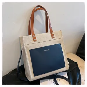 Detailed close-up of a canvas tote bag with brown leather handles and dark blue front pocket